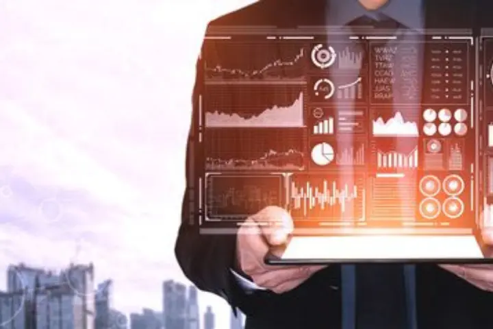 A person in a suit holds a tablet displaying digital financial charts and data visualizations, showcasing the power of Data Science, with a cityscape in the background.