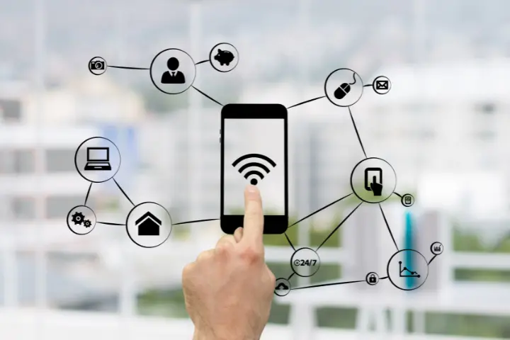 A hand touches a smartphone screen with a Wi-Fi symbol, surrounded by icons representing various connected devices and services, symbolizing smart technology and connectivity.